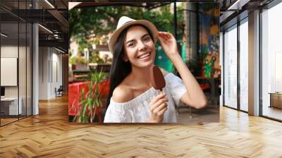 Beautiful young woman holding ice cream glazed in chocolate on city street Wall mural