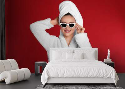 Beautiful young woman in bathrobe and sunglasses on red background Wall mural