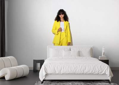 Beautiful young woman in stylish yellow suit and sunglasses near light wall Wall mural