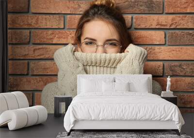 Beautiful young woman in warm sweater near brick wall Wall mural