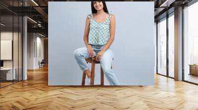 Beautiful young woman sitting on stool against light grey background Wall mural