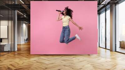 Beautiful young woman with microphone singing and jumping on pink background Wall mural