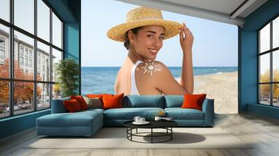 Beautiful young woman with sun protection cream on shoulder at beach Wall mural