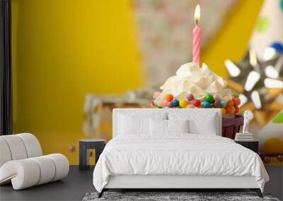 Birthday cupcake with burning candle and party cone on yellow table. Space for text Wall mural