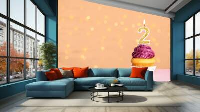 Birthday cupcake with number two candle on table against festive lights, space for text Wall mural