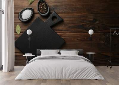 Black cutting board, salt, pepper and bay leaves on wooden table, flat lay. Space for text Wall mural