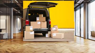 Black delivery van and many different parcels near yellow wall outdoors, space for text. Courier service Wall mural