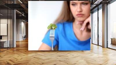 Blurred view of unhappy woman against light background, focus on fork with broccoli Wall mural