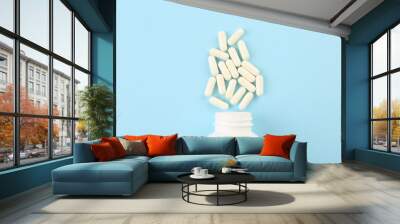 Bottle and vitamin capsules on light blue background, top view Wall mural