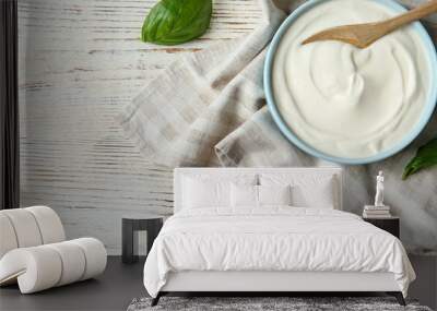 Bowl of sour cream with spoon and napkin on white wooden table, flat lay. Space for text Wall mural