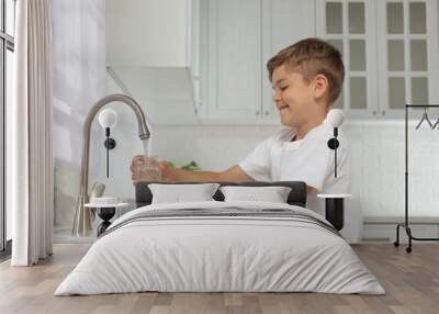 Boy filling glass with water from tap in kitchen Wall mural