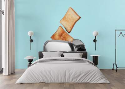 Bread slices popping up from modern toaster on light blue background Wall mural