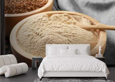 Buckwheat flour in bowl with wooden spoon on black table, closeup Wall mural