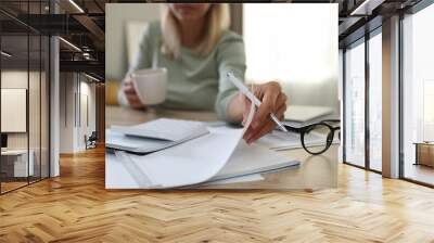 Budget planning. Woman with cup of drink and document at table indoors, closeup Wall mural