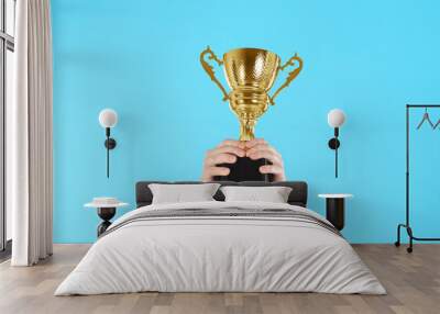 Businessman holding gold trophy cup on light blue background, closeup Wall mural