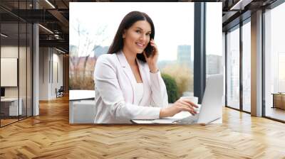 Businesswoman with laptop talking on phone in outdoor cafe. Corporate blog Wall mural