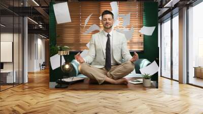 Calm businessman meditating on office desk in middle of busy work day Wall mural