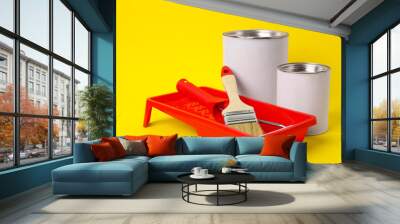 Cans of orange paint, brush, roller and container on yellow background Wall mural