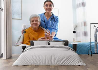 Care worker giving water to elderly woman in geriatric hospice Wall mural