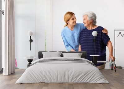 Caretaker helping elderly woman with walking frame indoors Wall mural