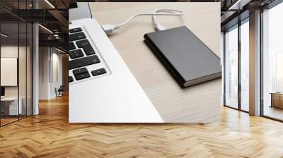 Charging modern laptop with power bank on wooden table, closeup Wall mural