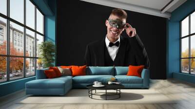 Charming young man wearing carnival mask on black background Wall mural