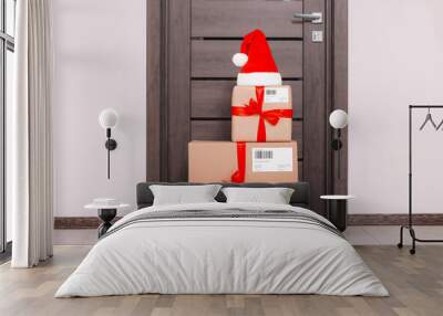 Christmas gift boxes and Santa hat near door indoors. Sending present by mail Wall mural