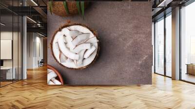 Coconut pieces in nut shell on brown table, flat lay. Space for text Wall mural