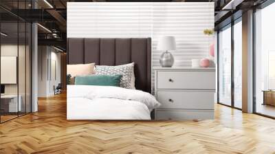 Comfortable bed with cushions, lamp and different decor on white chest of drawers in room. Stylish interior Wall mural