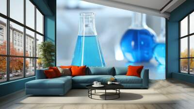 Conical flask with light blue liquid on table in laboratory. Space for text Wall mural