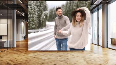 Couple walking near snowy forest, space for text. Winter vacation Wall mural