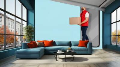 Courier with parcel walking out from huge smartphone on light blue background. Delivery service. Space for text Wall mural