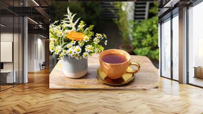 Cup of delicious chamomile tea and fresh flowers outdoors on sunny day Wall mural