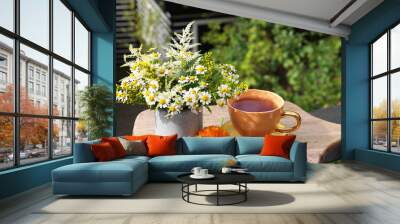 Cup of delicious chamomile tea and fresh flowers outdoors on sunny day Wall mural