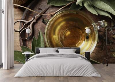 Cup of sage tea and green leaves on wooden tray, top view Wall mural