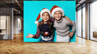 Cute children in warm sweaters and Christmas hats on color background Wall mural