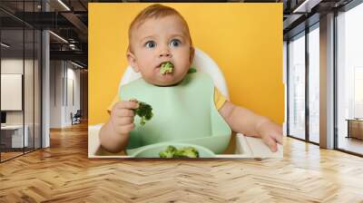 Cute little baby wearing bib while eating on yellow background Wall mural