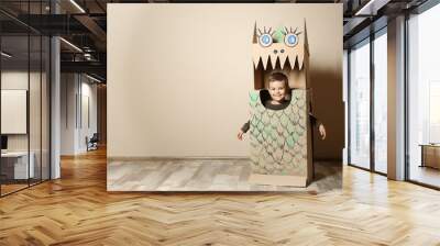 Cute little boy in cardboard costume of dinosaur near color wall. Space for text Wall mural