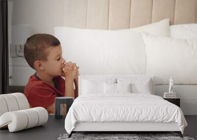 Cute little boy with hands clasped together saying bedtime prayer at home. Space for text Wall mural