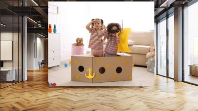 Cute little children playing with cardboard ship and binoculars at home Wall mural