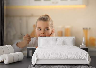 Cute little girl eating tasty pasta at table in kitchen Wall mural