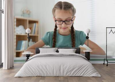 Cute little girl reading book at desk in room Wall mural