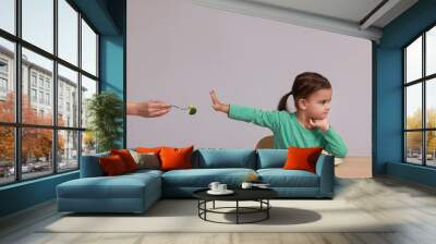 Cute little girl refusing to eat vegetables at table on grey background Wall mural