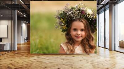 Cute little girl wearing wreath made of beautiful flowers in field Wall mural