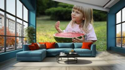 Cute little girl with half of juicy watermelon on green grass outdoors Wall mural