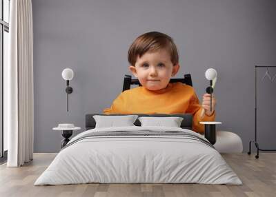 Cute little kid with spoon sitting in high chair on light grey background Wall mural