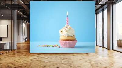 Delicious birthday cupcake with candle on light blue background Wall mural