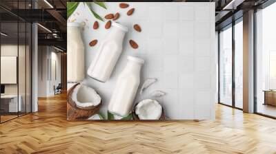 Different types of vegan milk in bottles with ingredients and green leaves on white tiled table, flat lay. Space for text Wall mural