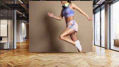 Digital composite of highlighted bones and woman in sportswear with headphones running on beige background Wall mural