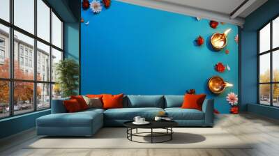 Diwali celebration. Diya lamps and beautiful flowers on blue background, flat lay. Space for text Wall mural